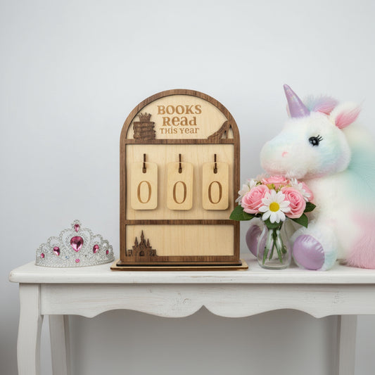 Wooden book tracker with unicorn plush toy and flowers on a white table